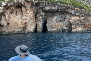 Tourist in the boat watching a cliffside cave with 2 narrow entrances
